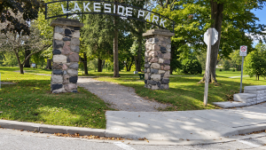 Stone entrance pillars supporting the Lakeside Park sign, with a shaded pathway and mature trees beyond